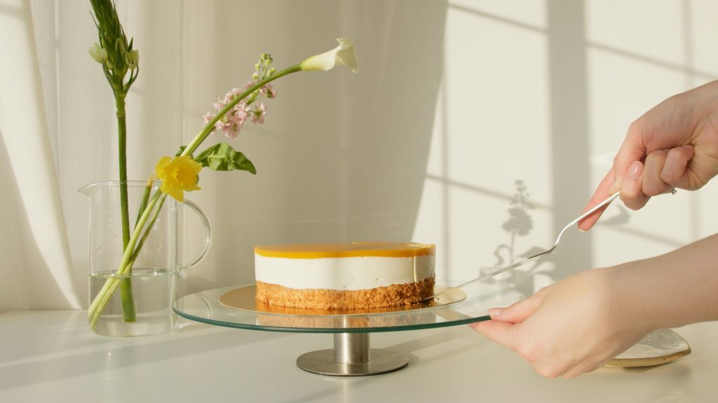 Elegante tarta de queso con limón sobre un soporte rodeado de flores naturales. Perfecta para celebraciones o proyectos culinarios.